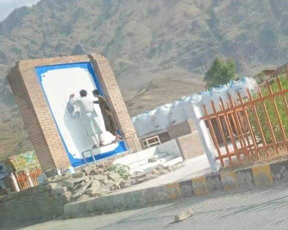 دو نفر در حال کشیدن پرچم طالبان روی تصویر پاک شده شاه امانالله خان در تورخم